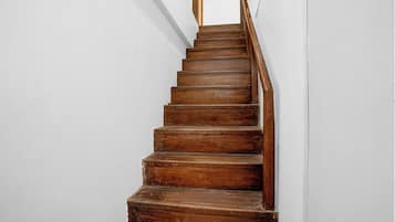 Una escalera de madera con barandilla que asciende frente a una pared lisa.