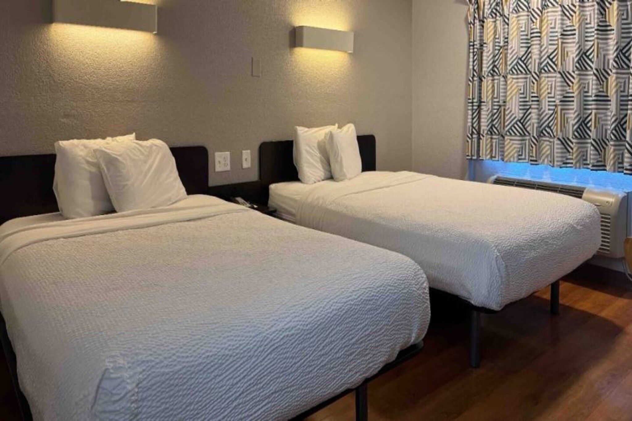 Habitación de hotel con dos camas, una ventana con cortinas estampadas y un calentador instalado en la pared.