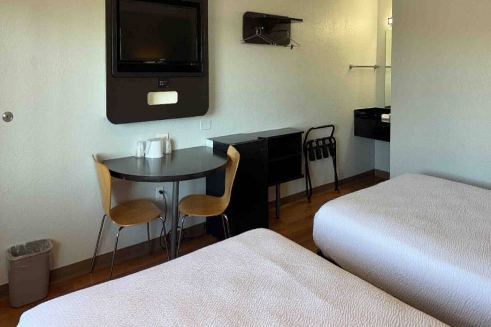 A hotel room with two beds, a desk with chairs, a television, and a small trash bin.