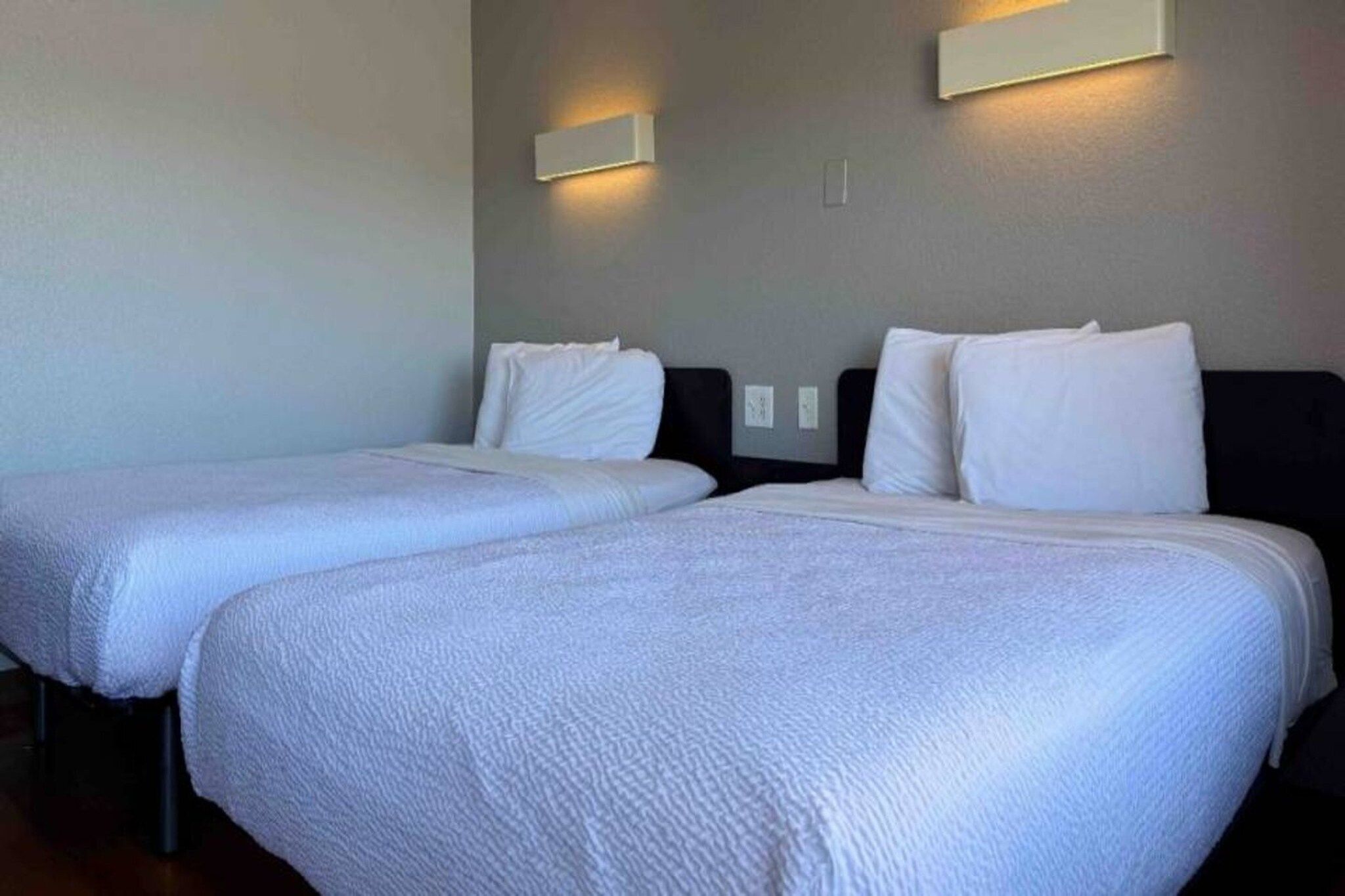 A hotel room with two beds, each with white bedding and headboards.