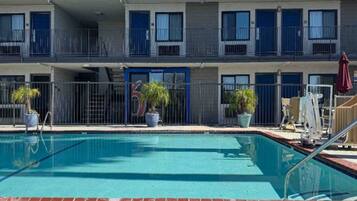 A hotel with a swimming pool, balconies with railings, and potted plants.