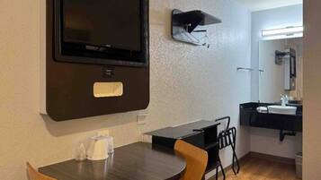 A compact room with a television mounted on the wall, a small table with chairs, a sink, and a mirror in the corner.