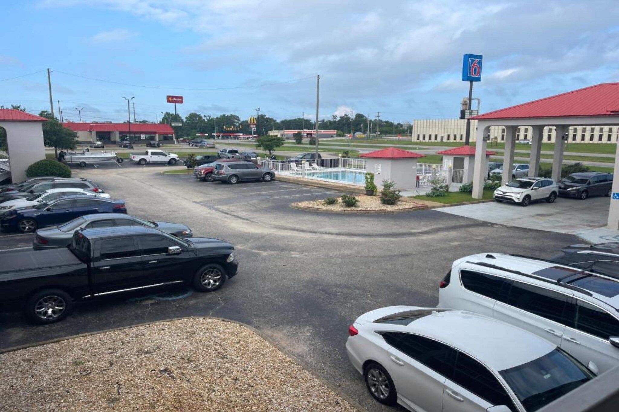 Um estacionamento com vários carros, um posto de gasolina e um edifício com telhado vermelho.