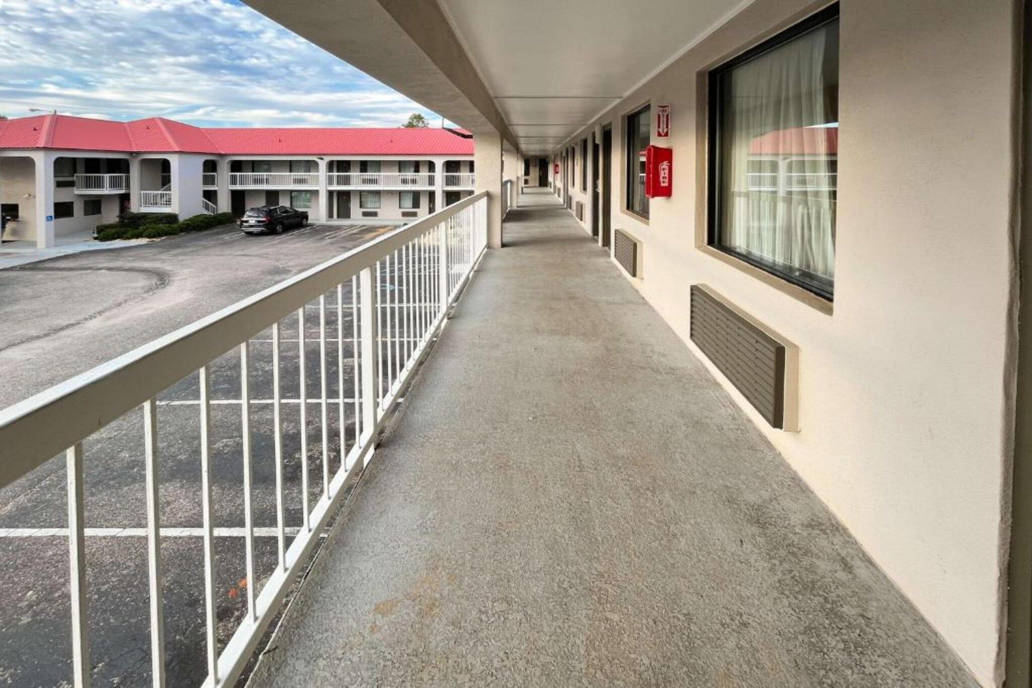 Corredor de hotel com uma varanda, um prédio de telhado vermelho ao fundo e um extintor de incêndio na parede.