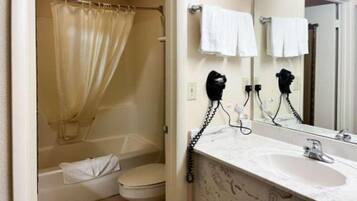 Ein Badezimmer mit Badewanne, Toilette und Waschbecken inklusive Spiegel. Zwei Haartrockner befinden sich an der Wand.