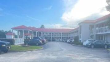 A hotel with a red-roofed building, a parking lot, and several cars parked in front.