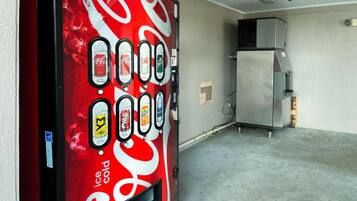 Ein Getränkeautomat mit verschiedenen Auswahlmöglichkeiten, ein Kühlschrank und ein Betonboden in einem Raum.