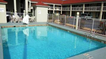 Ein Schwimmbecken mit umzäunter Terrassenfläche, umgeben von einem Gebäude mit rotem Dach.
