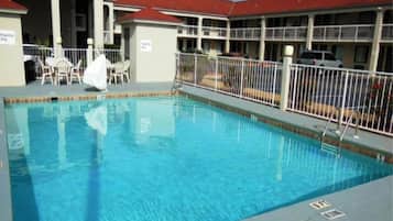 Piscina com área de deck cercada, rodeada por um edifício com telhado vermelho.