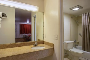 Un baño con lavamanos de encimera de granito, un espejo, inodoro y zona de ducha.