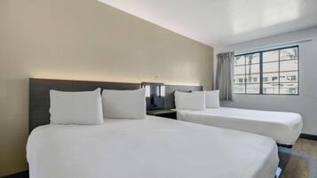 A hotel room with two beds, a nightstand, a lamp, and a window with curtains.