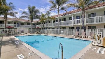 Hotel com piscina, várias varandas e palmeiras.