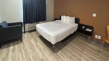 A hotel room with a bed, a chair, a desk, and a wall-mounted heater.