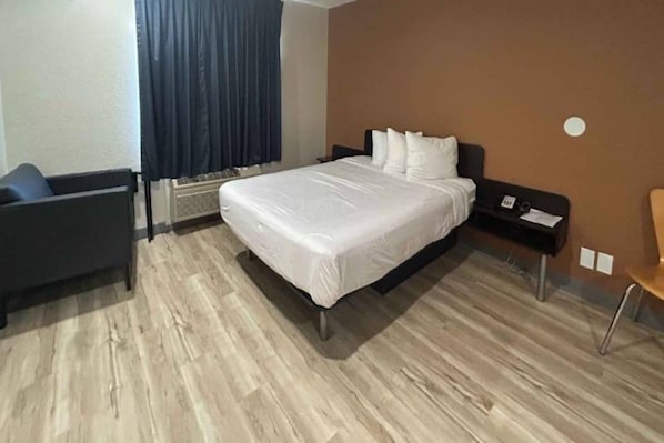 A hotel room with a bed, a chair, a desk, and a wall-mounted heater.