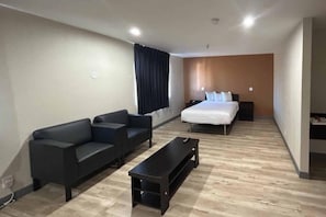 A hotel room with a sofa set, a bed, a small table, and a nightstand.