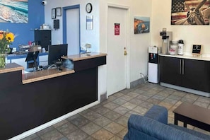A reception area with a desk, computer, and a clock on the wall. There is a door with a sign, a painting of a coastal scene, and a water dispenser.