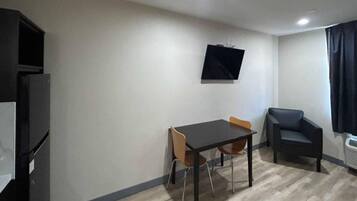 Una stanza piccola con un tavolo, due sedie, una TV a muro e un divano.