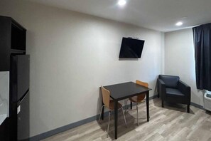 Een kleine kamer met een tafel, twee stoelen, een aan de muur bevestigde televisie en een bank.