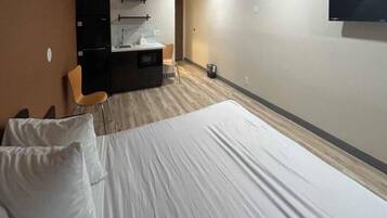 A hotel room with a bed, a desk, a chair, and a television.