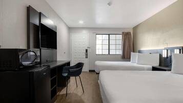 A hotel room with a desk, chair, two beds, a TV, and a window with curtains.
