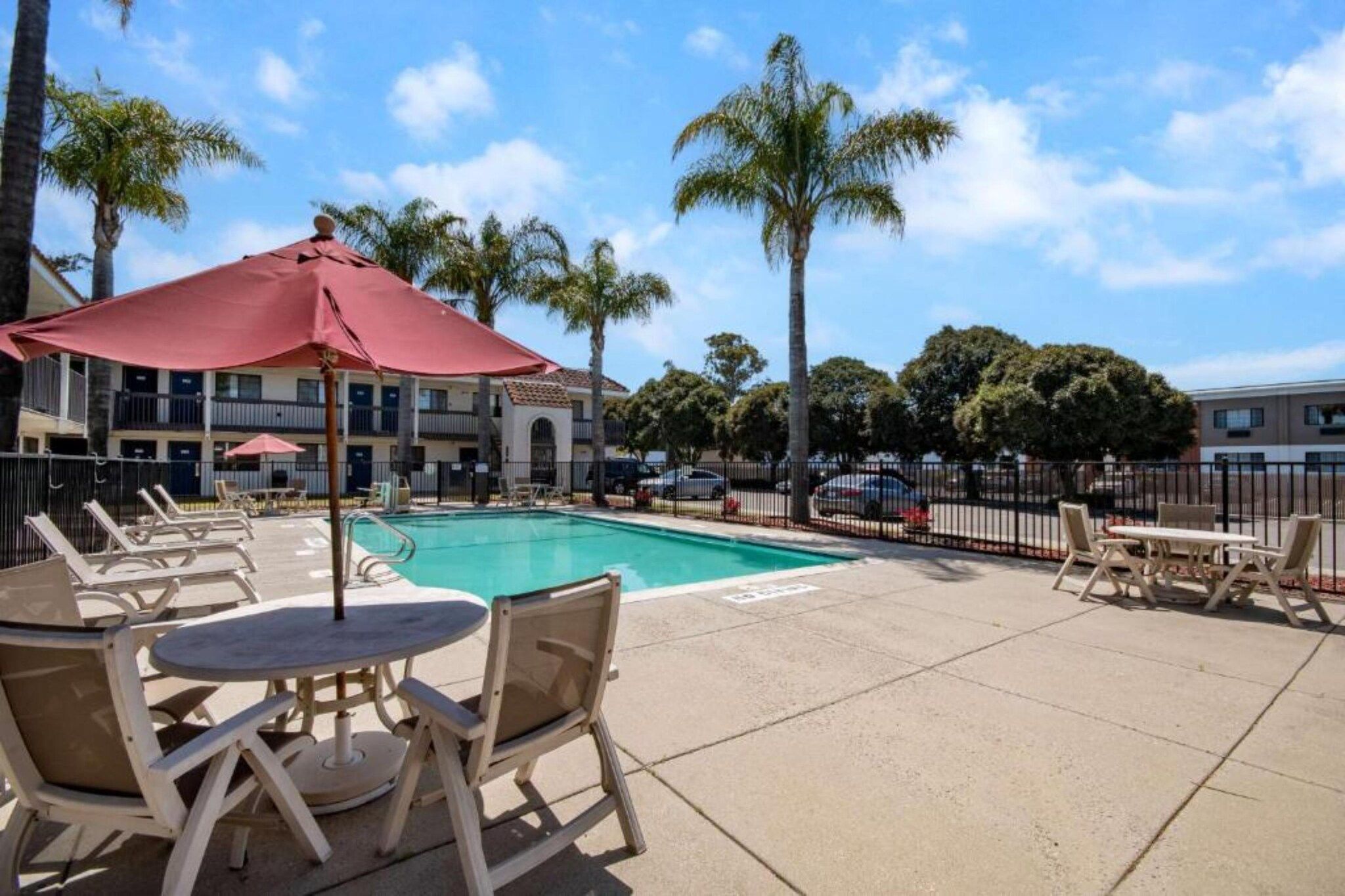 A pool area with lounge chairs and umbrellas, surrounded by palm trees and a building with multiple windows.