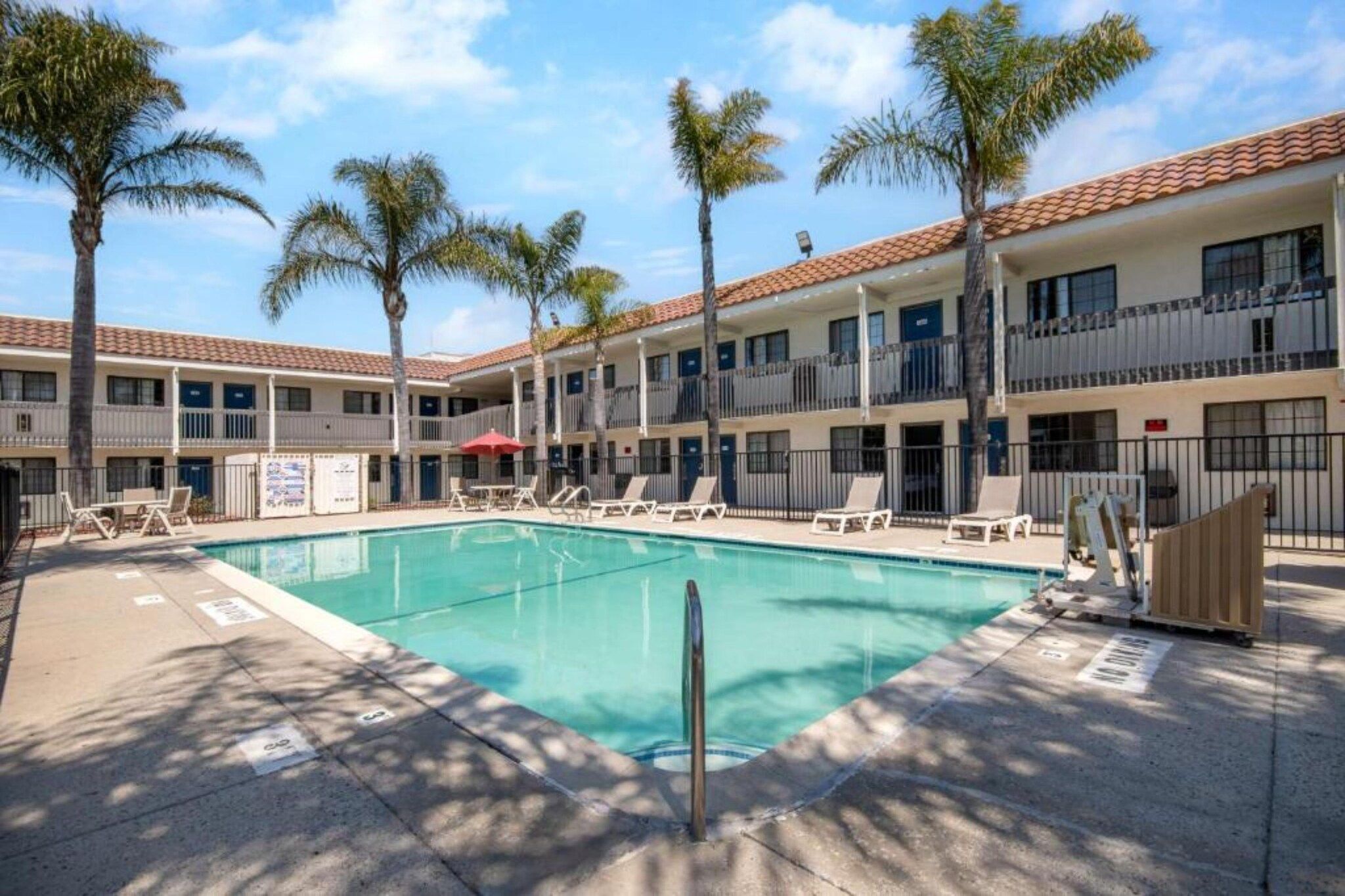 A hotel with a swimming pool, palm trees, and a tiled roof.