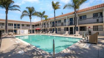 A hotel with a swimming pool, palm trees, and a tiled roof.