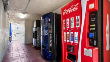 A row of vending machines with various beverage options, including Coca-Cola, in a corridor with tiled flooring.