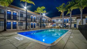 A hotel with a swimming pool, palm trees, and multiple balconies.