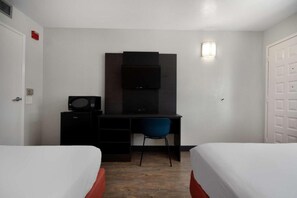 Habitació d'hotel amb dos llits, una taula de treball amb cadira, microones, televisió i una làmpada petita penjada a la paret.