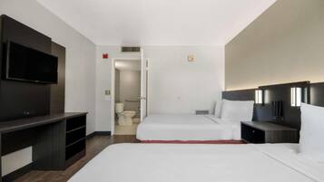 A hotel room with a large bed, a desk, a TV, and a bathroom visible through an open door.
