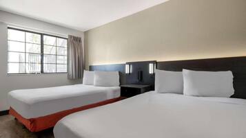 Quarto de hotel com duas camas, uma mesa de cabeceira, uma luminária e uma janela com cortinas.