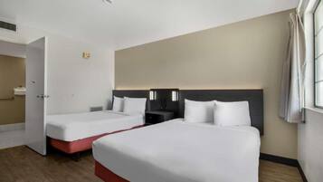 A hotel room with two beds, a nightstand, and a bathroom door.