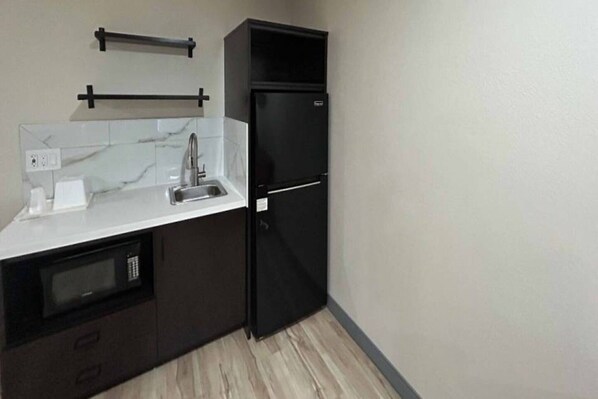 A compact kitchen with a built-in microwave, a sink, and a black refrigerator.