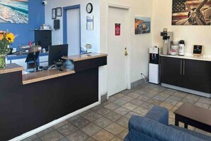 A reception area with a desk, computer, and a clock on the wall. There is a door with a sign, a water dispenser, and a small table with a chair.