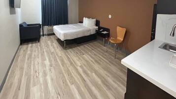 Une chambre d’hôtel avec un lit, une chaise, un bureau avec un lavabo et une fenêtre avec des rideaux.