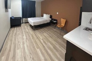 Een hotelkamer met een bed, een stoel, een bureau met een wastafel en een raam met gordijnen.