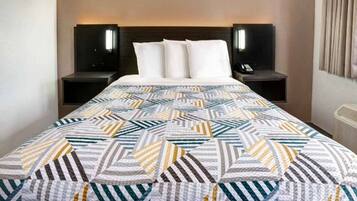 A hotel room with a bed, two bedside tables, and a wall-mounted air conditioning unit.