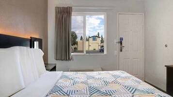Une chambre d’hôtel avec un lit, une fenêtre avec des rideaux, une porte et une vue sur un bâtiment à l’extérieur.