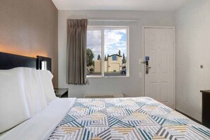Een hotelkamer met een bed, een raam met gordijnen, een deur en uitzicht op een gebouw.