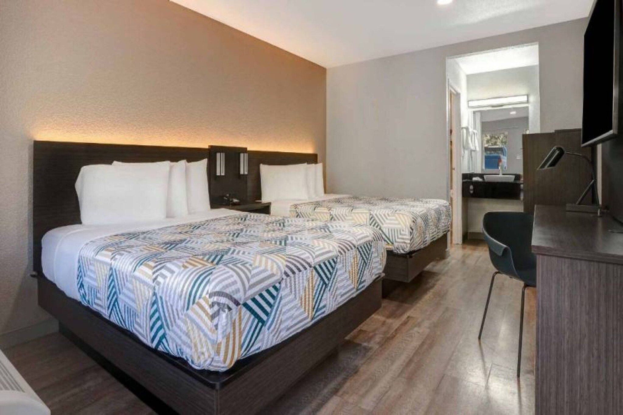 A hotel room with two beds, a desk, and a television.