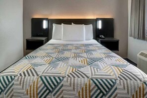 A hotel room with a bed, two bedside tables, and a wall-mounted air conditioning unit. - 1 Full Bed | ADA/RI Shower/Mini Fridge (Rancho Cordova)