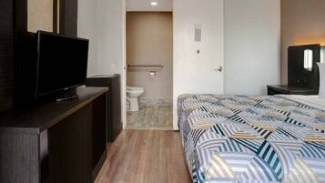 A hotel room with a bed, a television on a stand, a bathroom with a toilet and shower, and a door leading to another room.