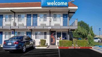 A two-story motel with a 'Welcome' sign, a parking lot, and a 'No Parking Fire Lane' sign.