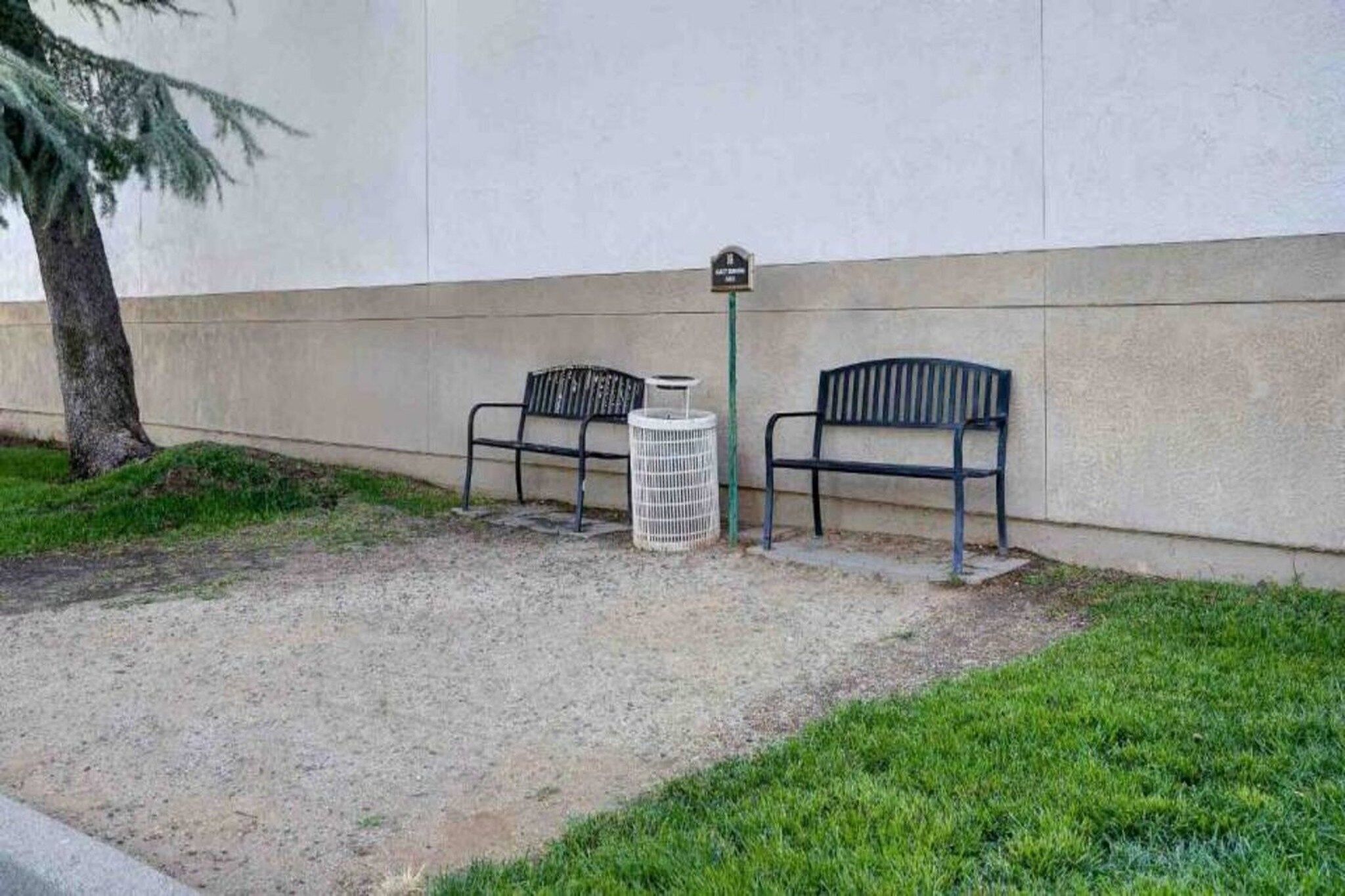 Two metal benches and a trash can against a wall.