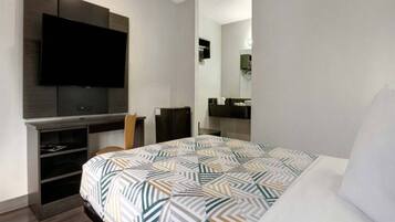 A hotel room with a bed, a TV mounted on the wall, a desk, and a chair.