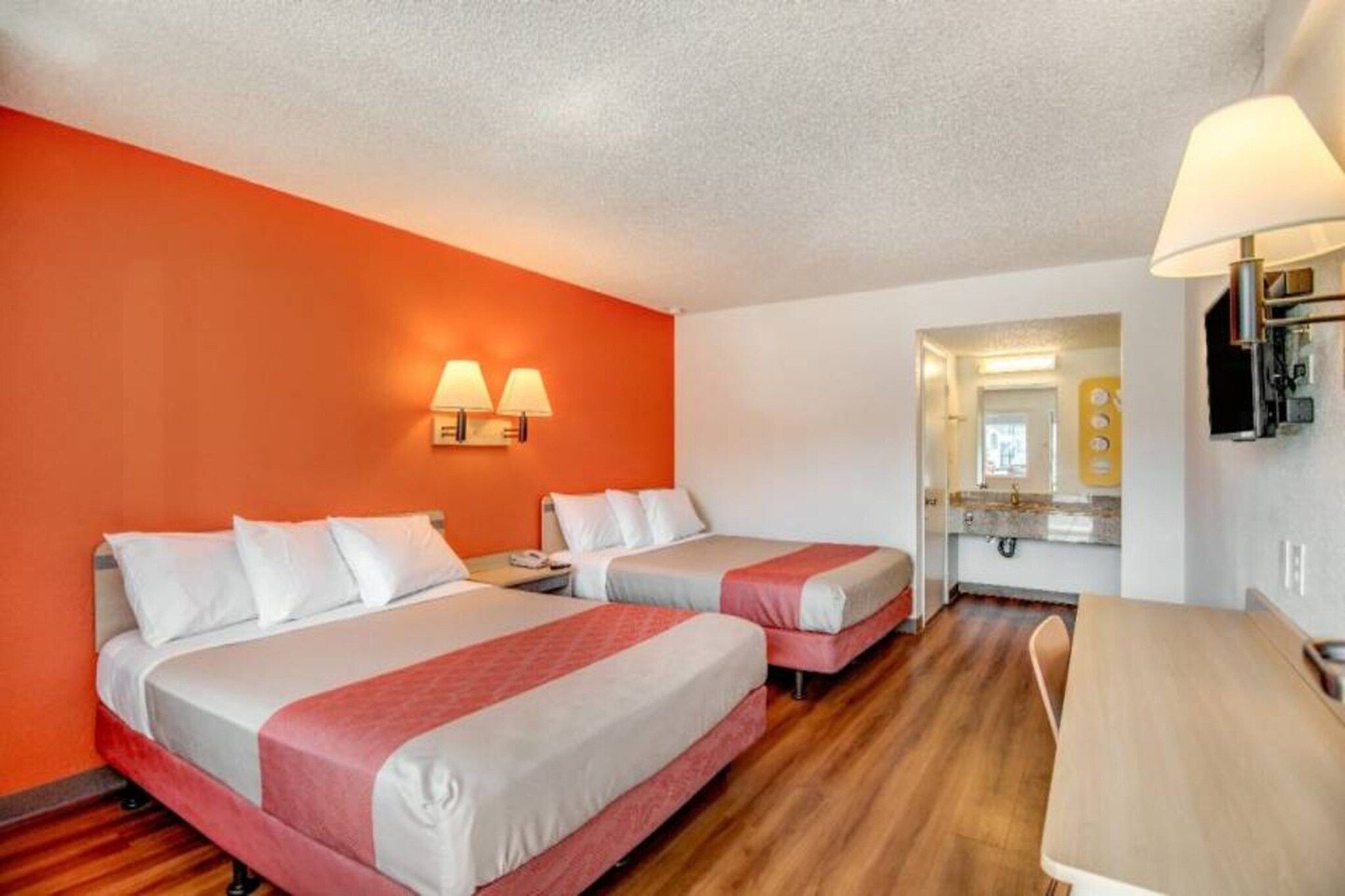 A hotel room with two beds, a desk, a chair, a mirror, and a lamp.