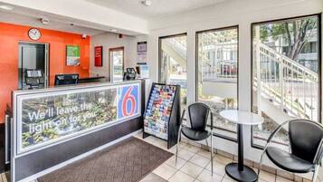 A hotel reception area with a counter, a clock, a magazine rack, and two chairs.