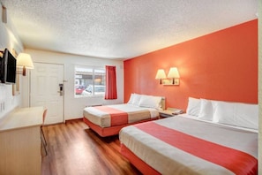 A hotel room with two beds, a desk, a chair, and a window with a view of parked cars. - 2 Queen Beds | Micfridge (Stockton)