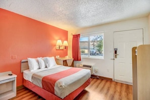 A hotel room with a bed, bedside table, lamp, window with curtains, and a door. - 1 Queen Bed | Non-Smoking (Stockton)